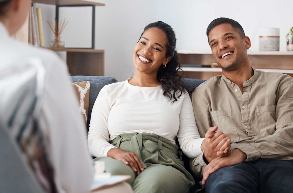 Smiling couple holding hands while meeting with a counselor
